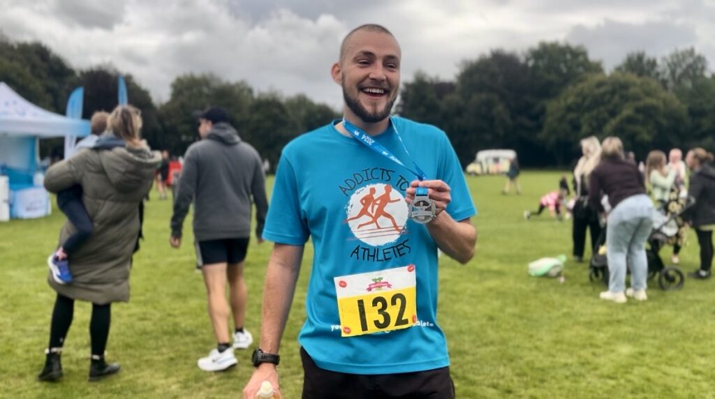 A man in running clothes with a medal around his neck. He is smiling.