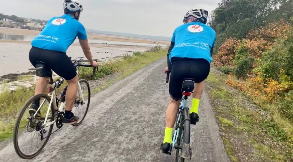 Two people in blue tops cycling along a path together.