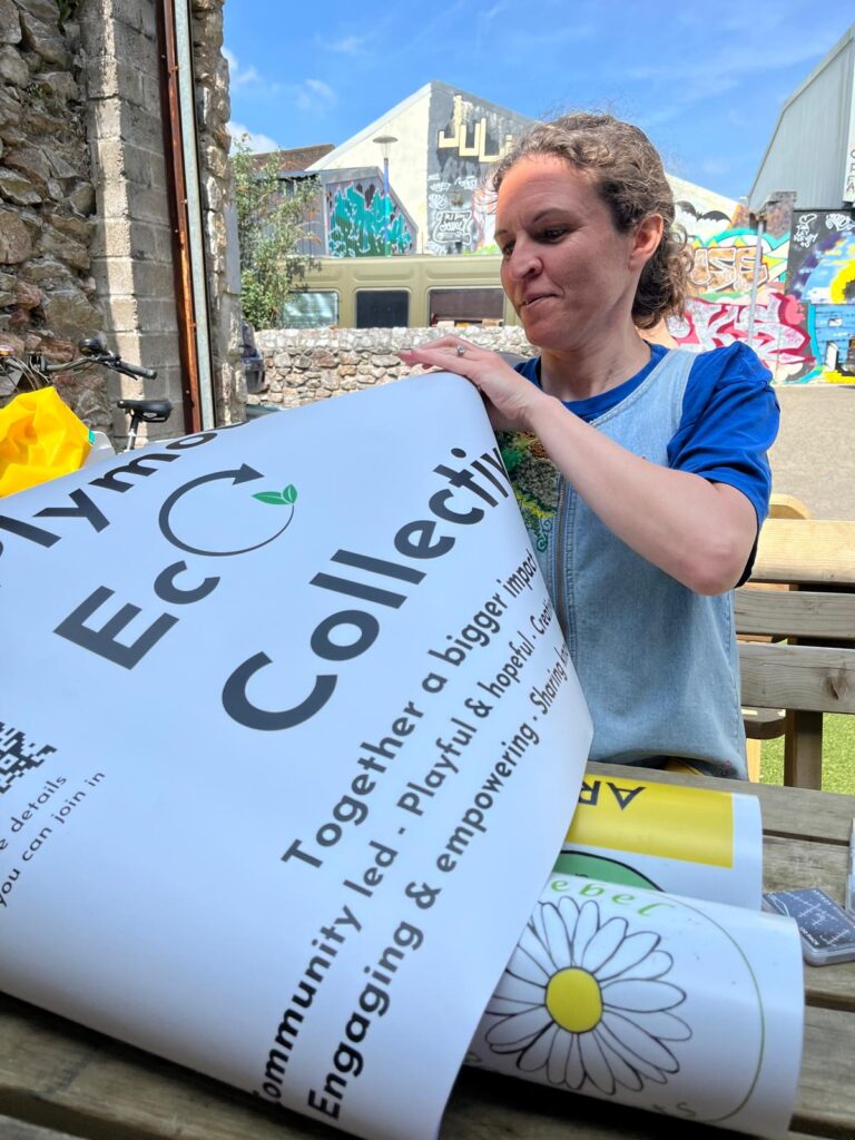 A woman unfolding a sign saying Plymouth Eco Collective