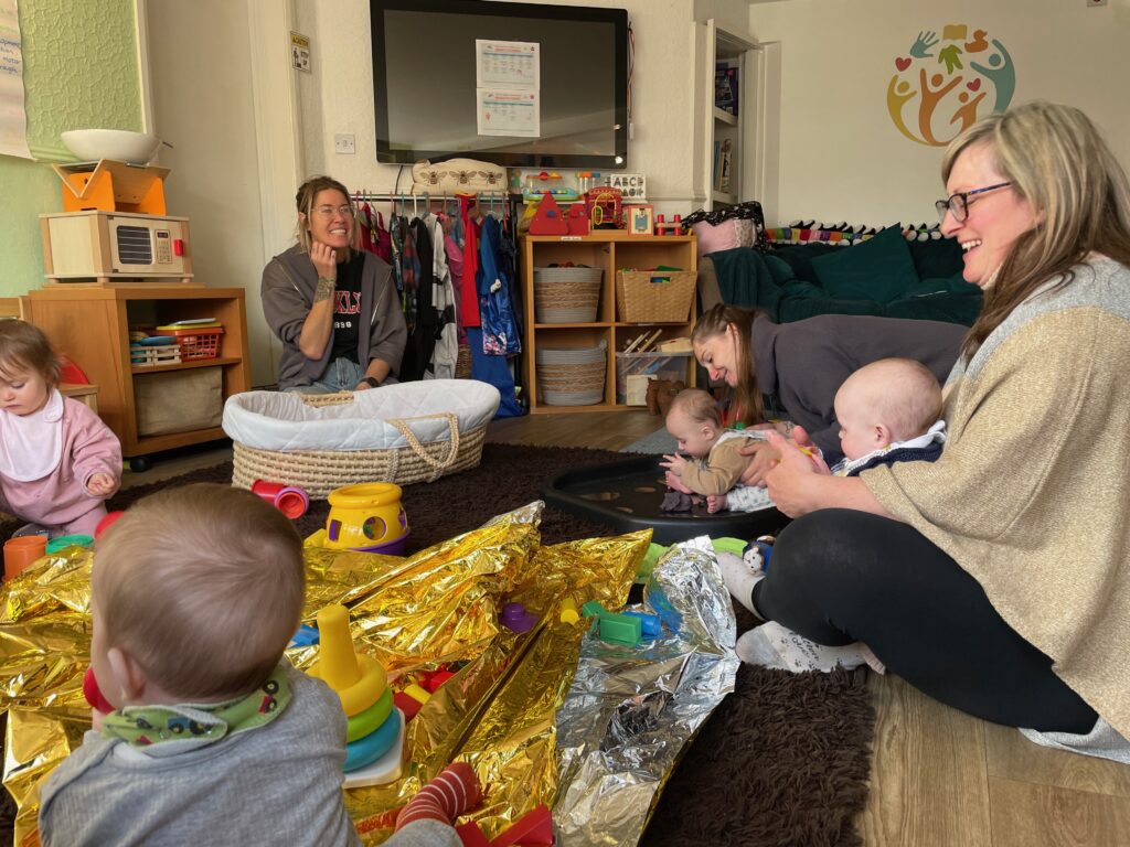 A groups of women and babies sitting in a circle with toys.