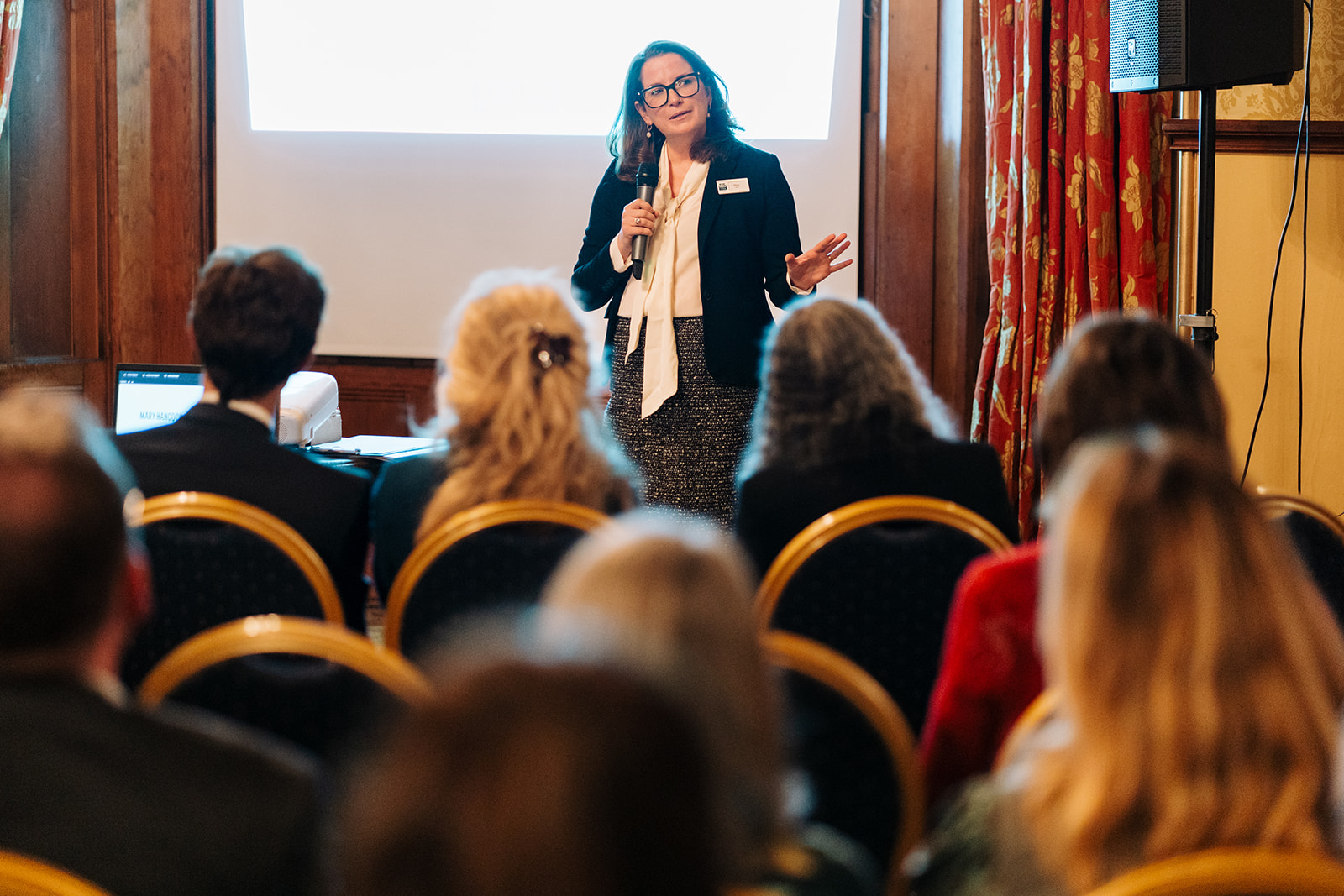 CEO Mary Hancock holding a microphone and standing in front of an audience.